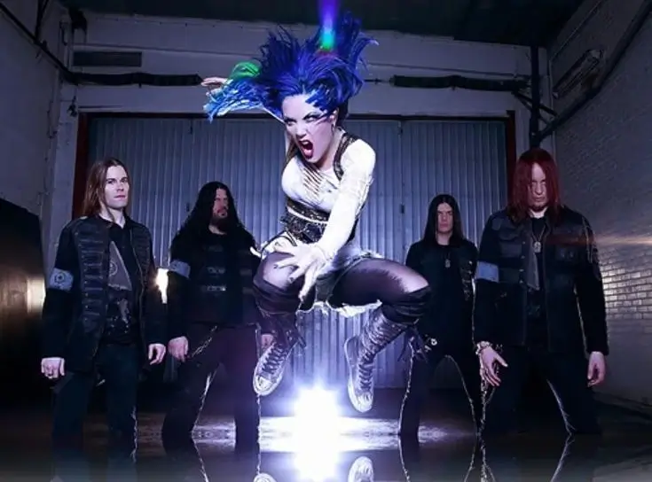 Arch Enemy band photo with Alissa White-Gluz jumping mid-air in front of four band members in a gritty industrial setting