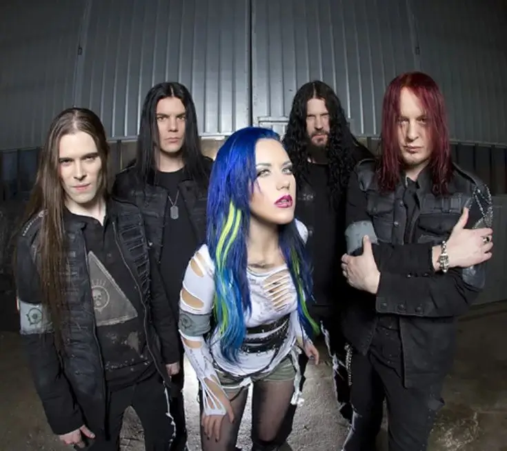 Arch Enemy band photo with Alissa White-Gluz in front, surrounded by four members in dark clothing standing against an industrial backdrop