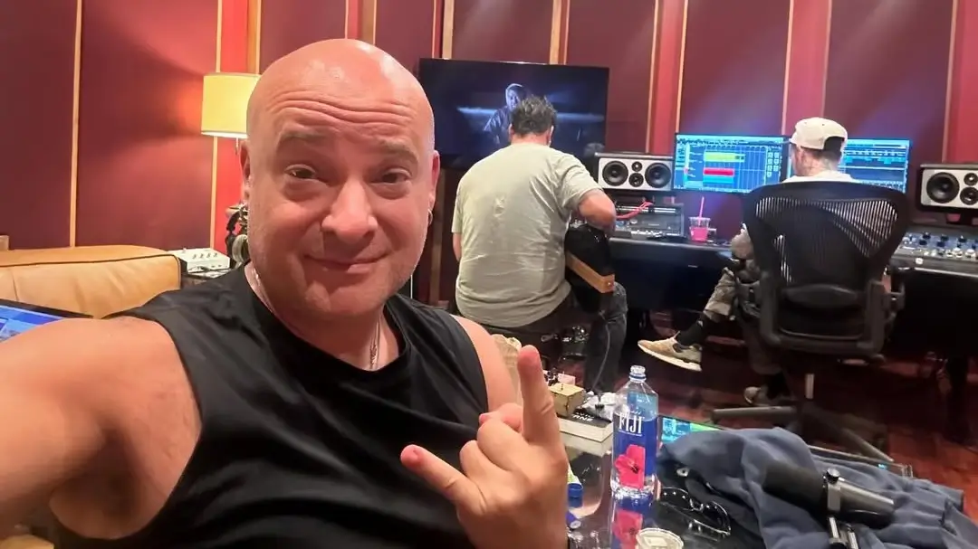 David Draiman of Disturbed in a recording studio, taking a selfie while two producers work on music in the background.