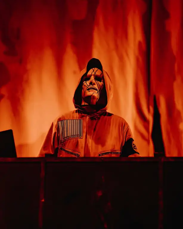 Jeff Karnowski of Slipknot in his signature hooded jumpsuit, standing behind his workstation with an intense atmosphere.