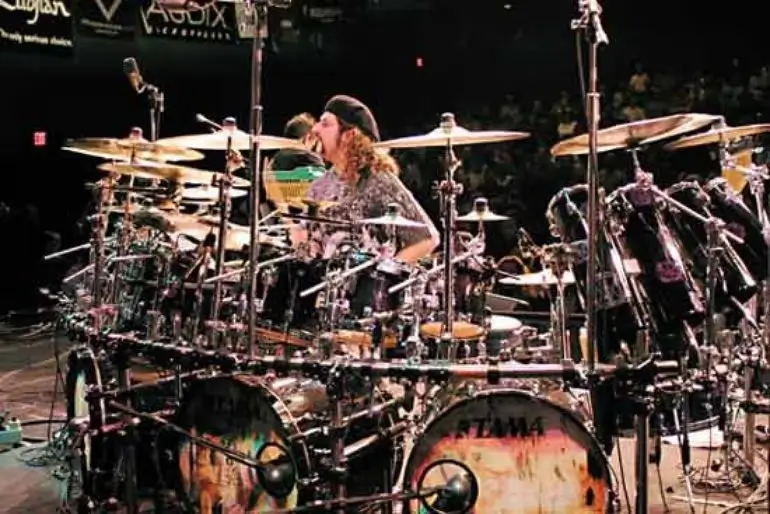 Mike Portnoy playing a massive Tama drum set on stage with intense focus.