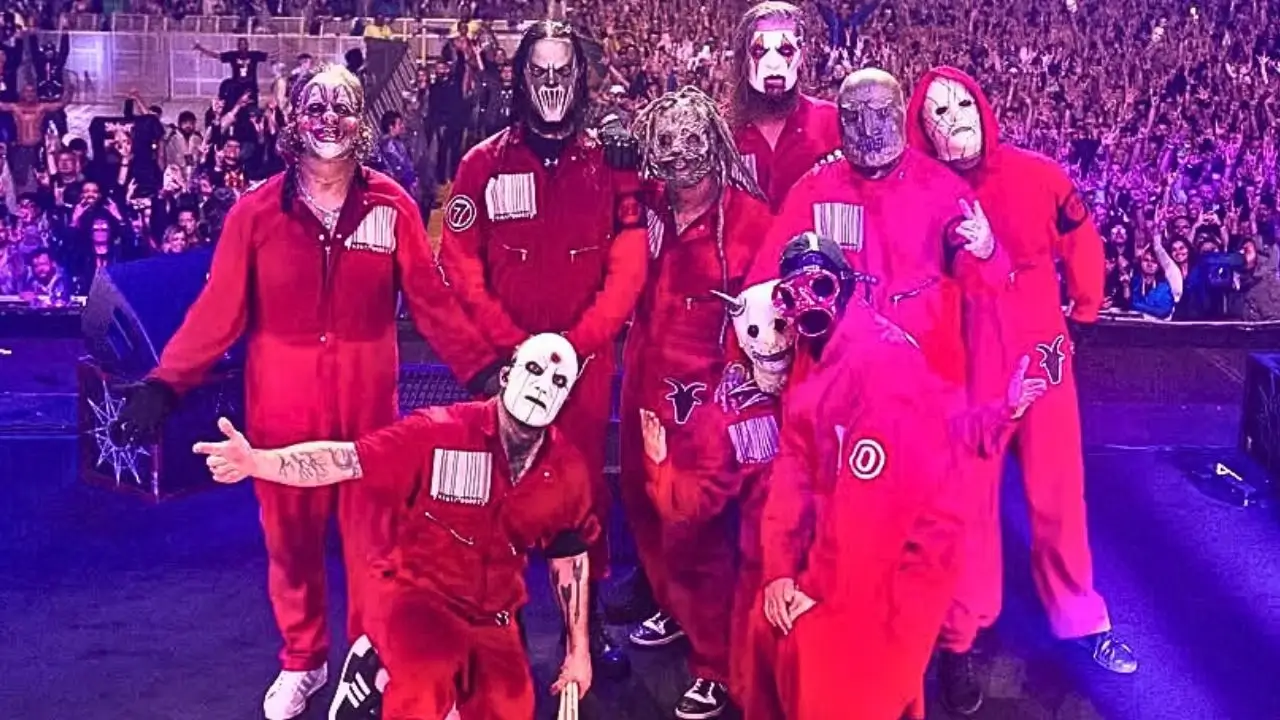 Slipknot band members in red jumpsuits and masks on stage with a cheering crowd in the background, 2024.