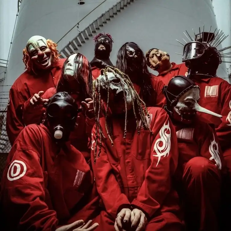 Slipknot members wearing signature red jumpsuits and horror-inspired masks, posing in a dramatic stance.