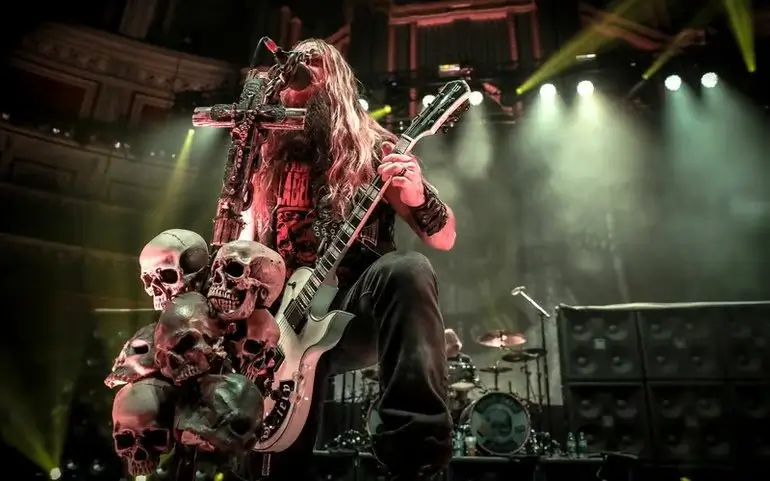 Zakk Wylde performing live on stage, surrounded by skulls, wielding his iconic bullseye Les Paul guitar.